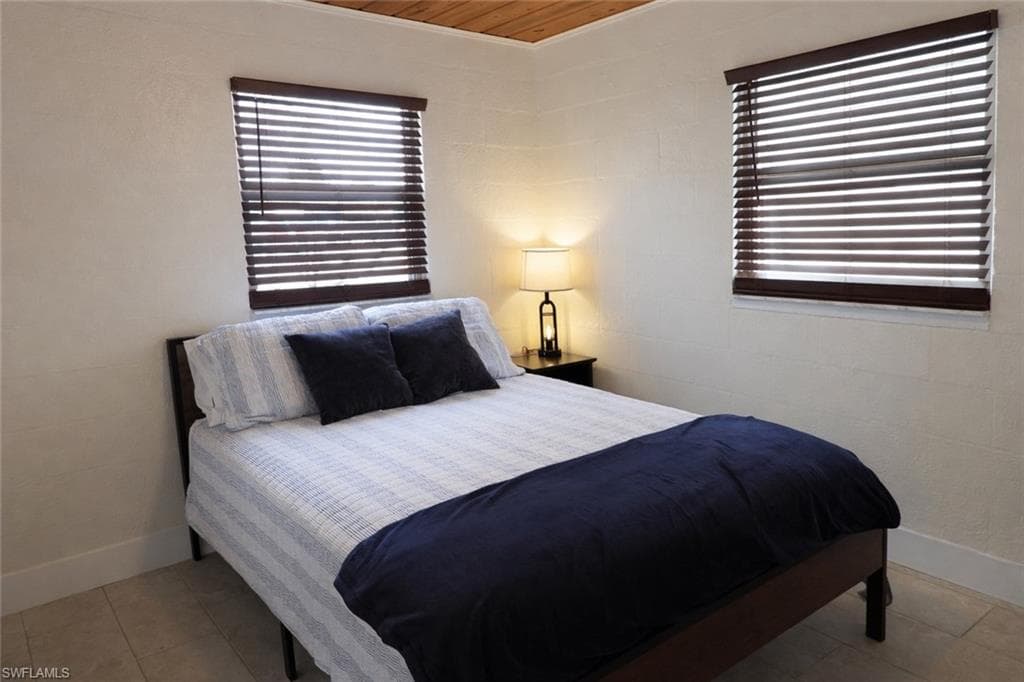 Bedroom featuring two windows with wood-finish blinds, light-toned walls, and a wood-panel ceiling