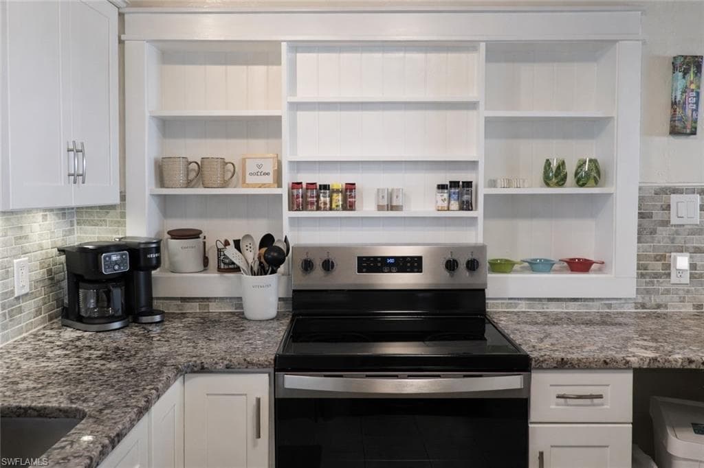Modern kitchen featuring white cabinetry, granite-finish countertops, stainless steel range, and a tiled backsplash