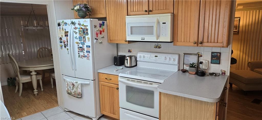 Kitchen featuring wood-finish cabinetry, white appliances, and a tiled backsplash