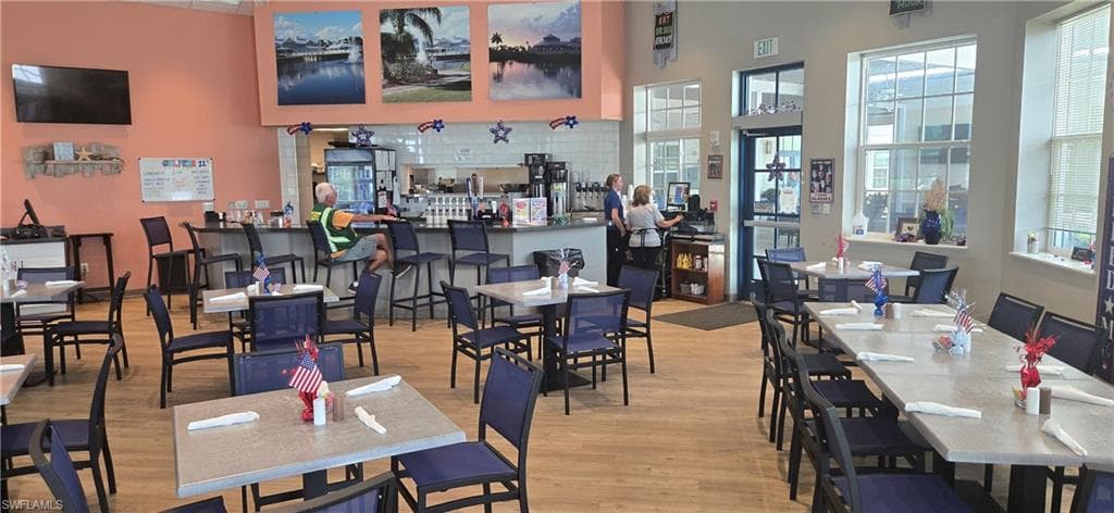 Spacious dining area featuring wood-finish flooring, a full-service bar with seating, multiple tables with chairs, and large windows providing natural illumination