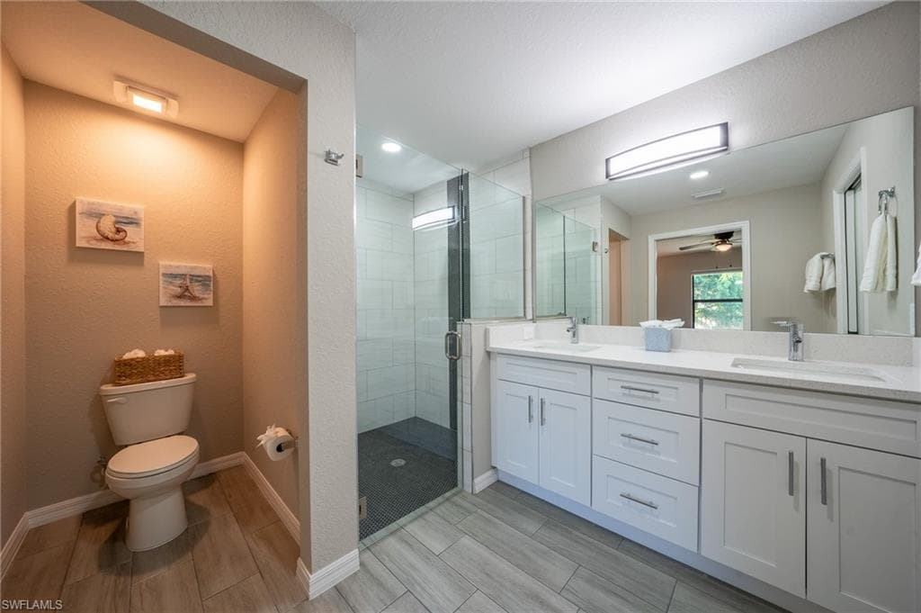 Modern bathroom featuring a dual vanity with white shaker-style cabinetry, a spacious glass-enclosed shower with subway tile surround, recessed lighting, and wood-finish flooring