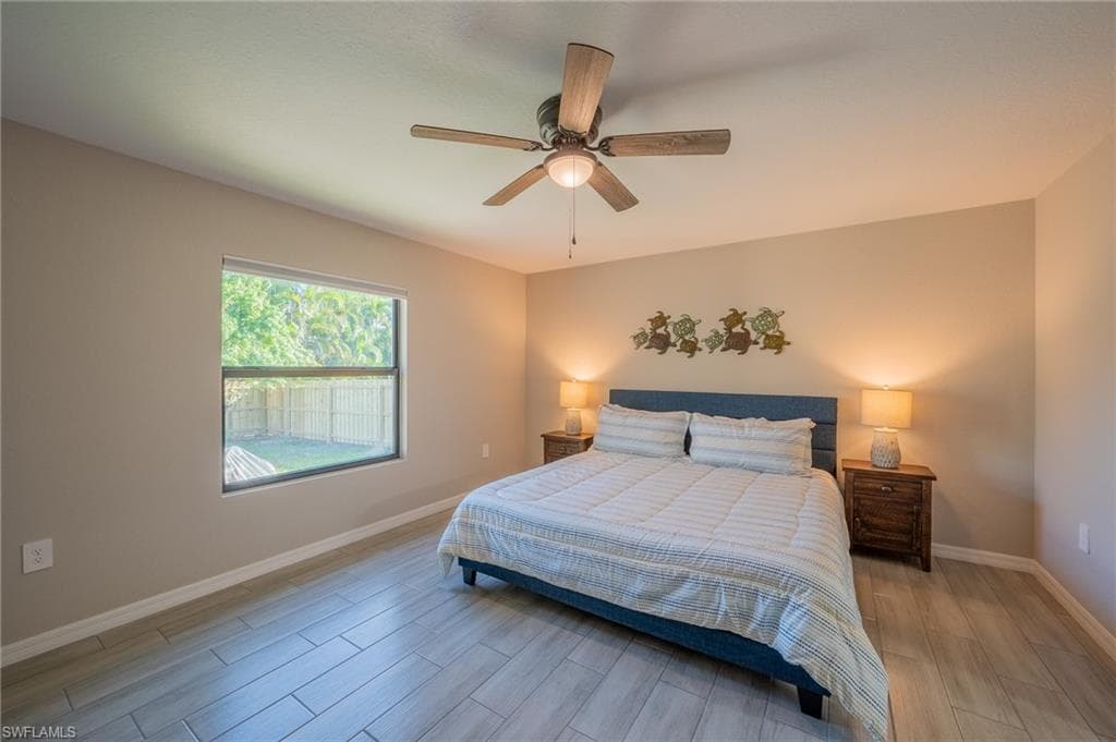 Bedroom featuring wood-finish tile flooring, a window offering exterior sightlines, and a ceiling fan with integrated lighting