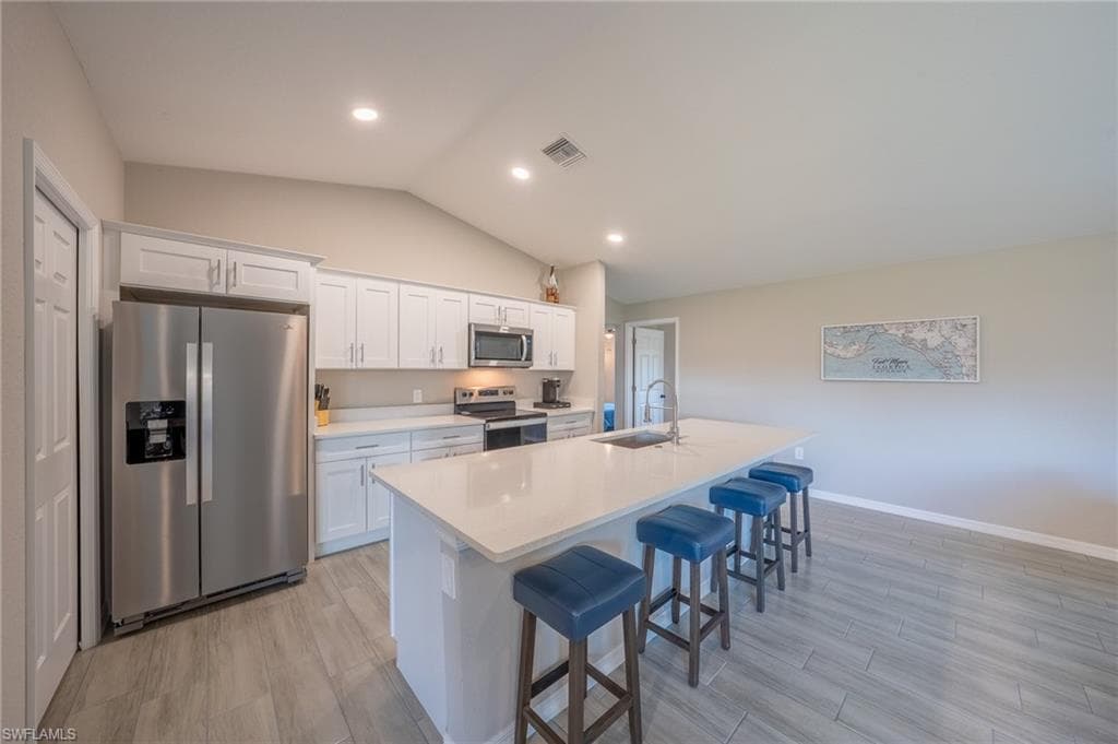 Modern kitchen featuring white shaker cabinetry, stainless steel appliances, a large center island with a sink, light-toned countertops, and wood-finish flooring