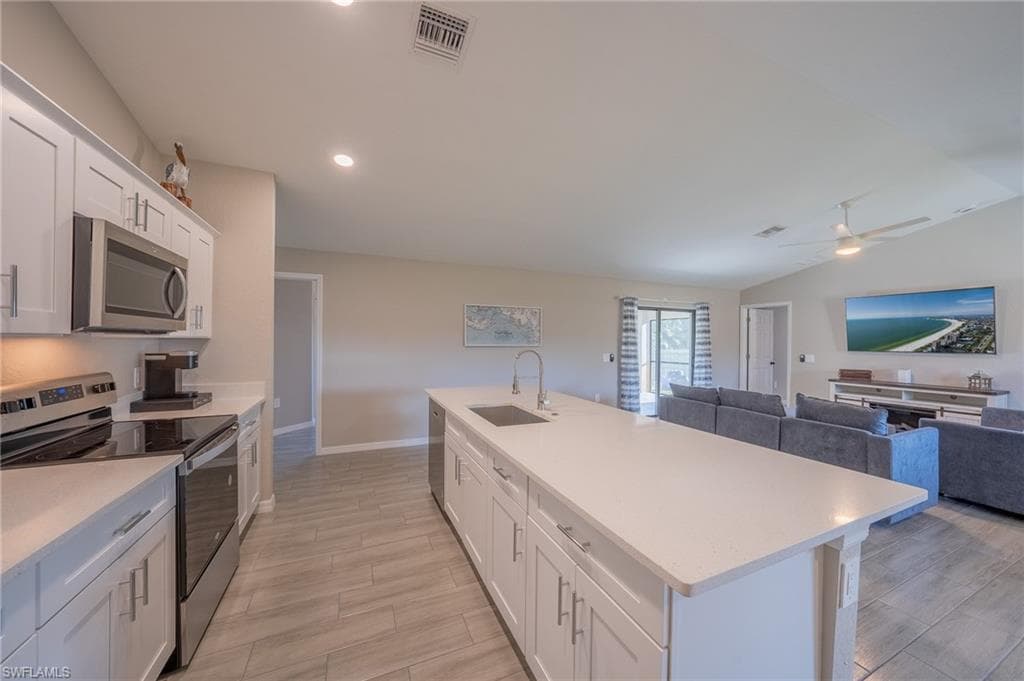 Open concept kitchen featuring white shaker cabinetry, stainless steel appliances, a large center island with an undermount sink, recessed lighting, and wood-finish tile flooring