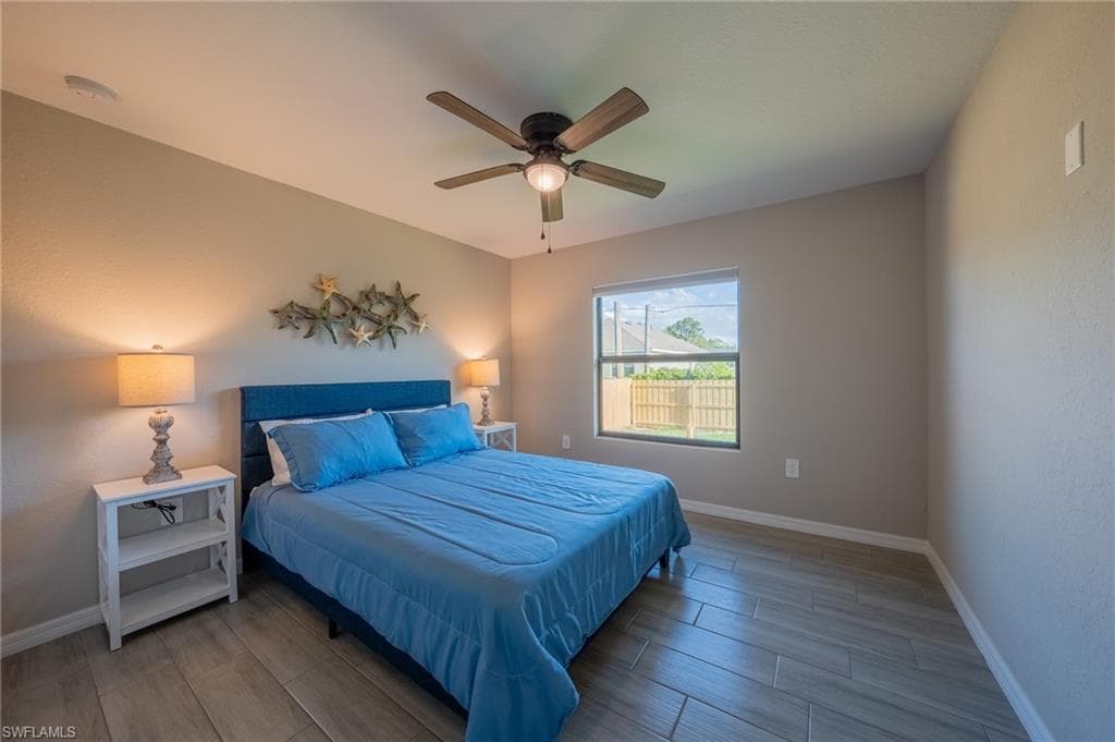 Spacious bedroom featuring wood-finish tile flooring, a window with exterior fencing, a ceiling fan with integrated lighting, and a neutral wall color