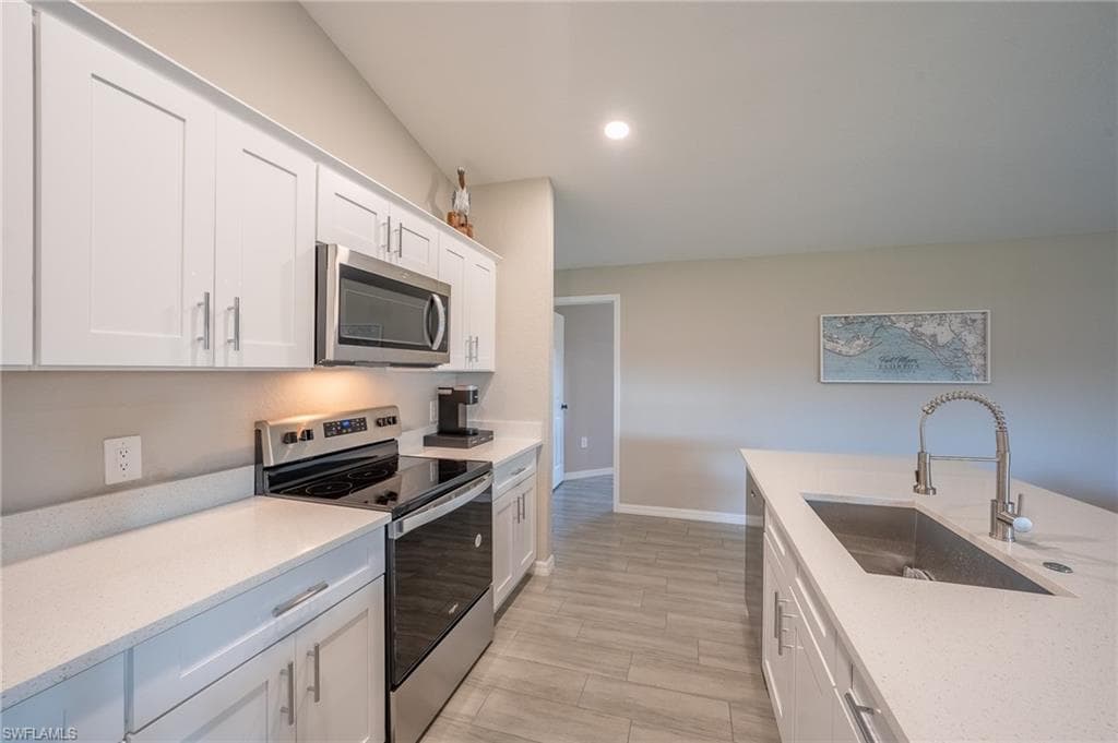 Kitchen featuring white shaker cabinetry, stainless steel appliances, light-toned countertops, and wood-finish tile flooring