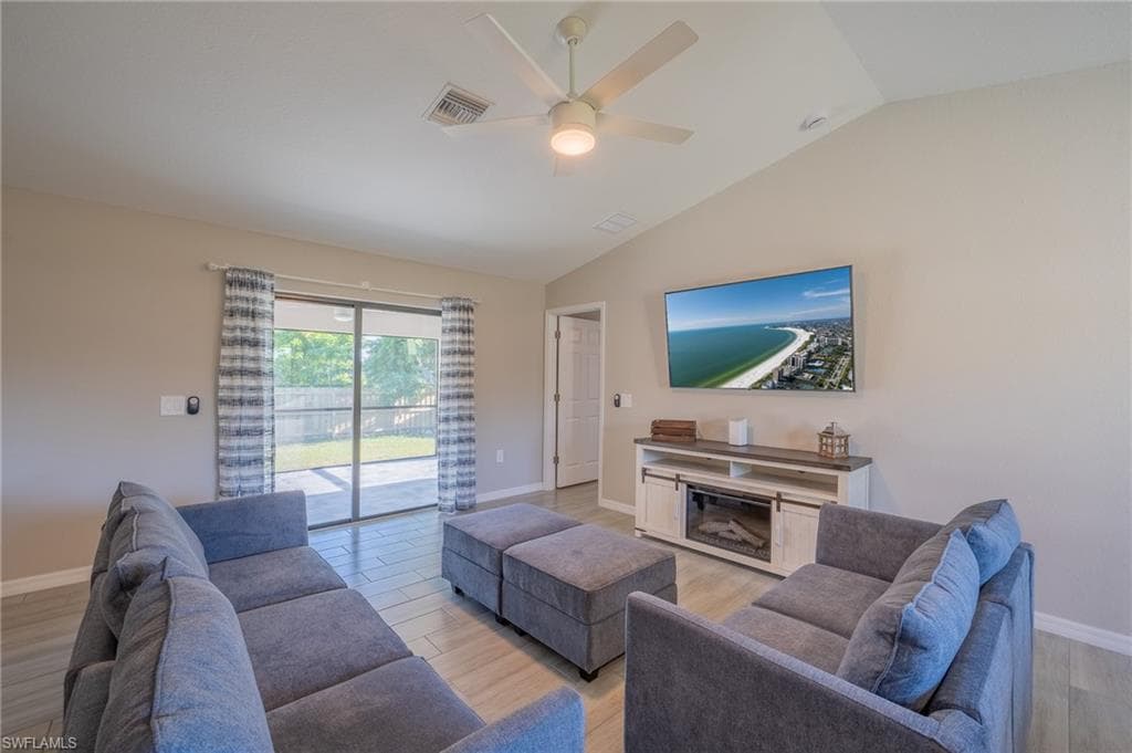 Vaulted ceiling living area featuring wood-finish flooring, a ceiling fan with integrated lighting, and sliding glass doors opening to a paved patio