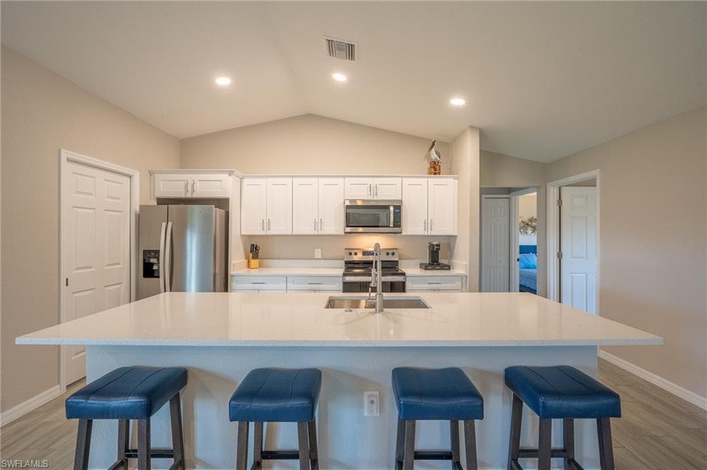 Modern kitchen featuring a large central island with seating, white shaker cabinetry, stainless steel appliances, and a vaulted ceiling with recessed lighting