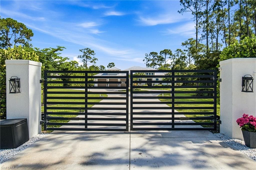 Custom motorized luxury Gated Entry is enhanced with tropical landscaping details and neatly maintained hedgerow across the frontage.