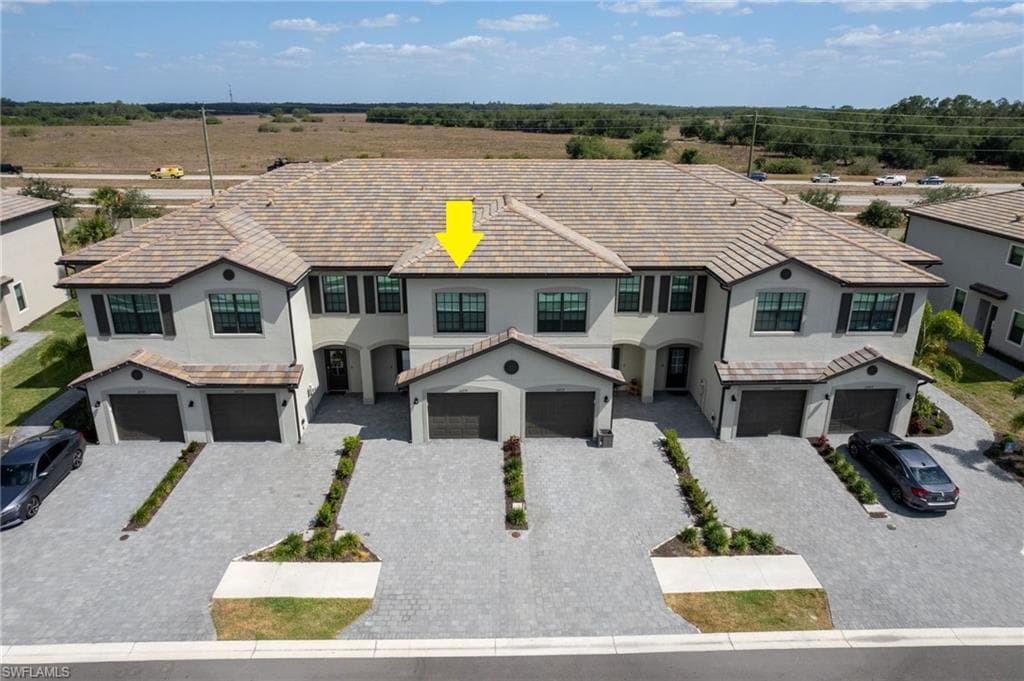 Aerial view highlighting the townhome’s attractive exterior, attached one-car garage, driveway parking for an additional vehicle, plus convenient guest parking nearby