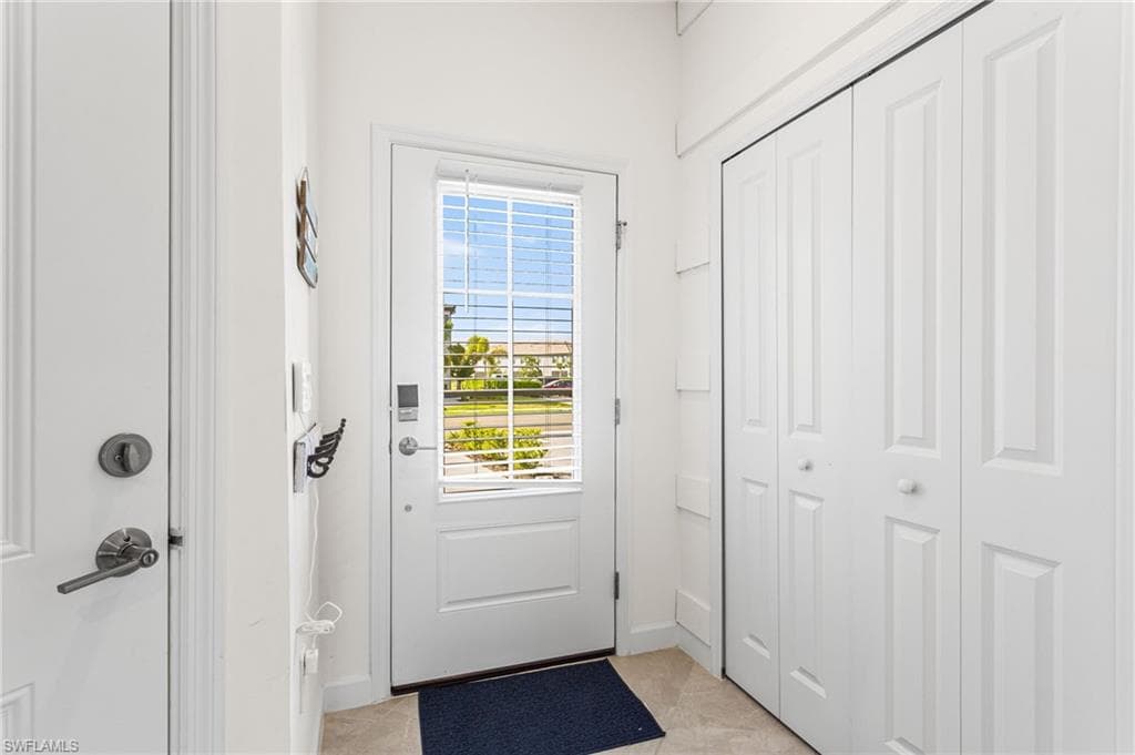 Step through a decorative front door with glass insert, equipped with a keyless entry pad and security camera, into a welcoming foyer featuring a coastal-inspired half bath and convenient storage