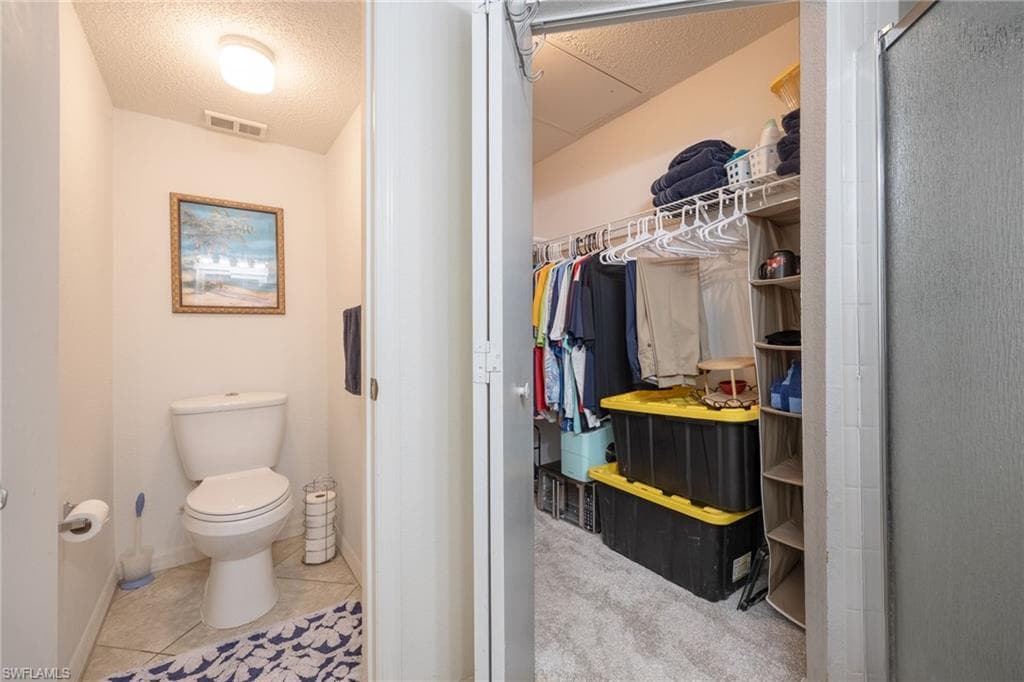 Powder room featuring tile flooring and an overhead light fixture, located beside a walk-in closet with carpet flooring and built-in wire shelving