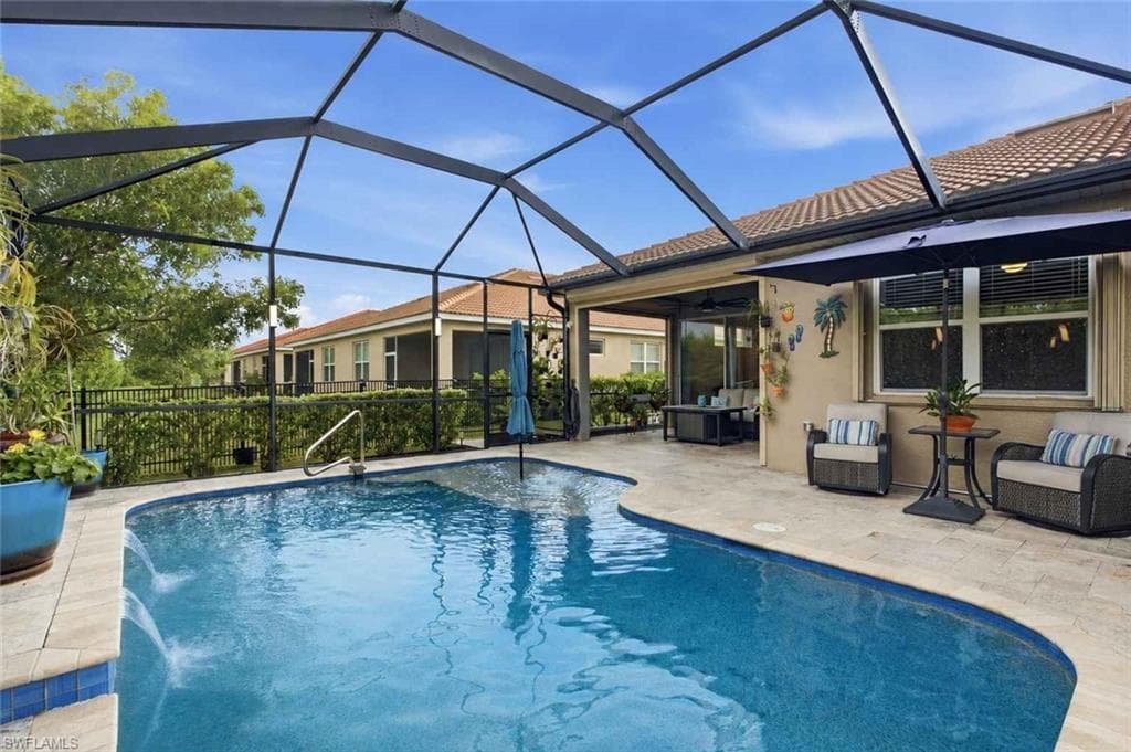 Screened-in outdoor pool area featuring a freeform swimming pool with water features, paver decking, and a covered lanai