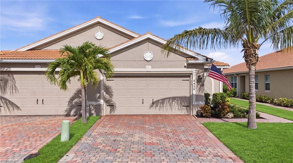 Stucco exterior featuring a two car garage, decorative gable vents, and a tile roof