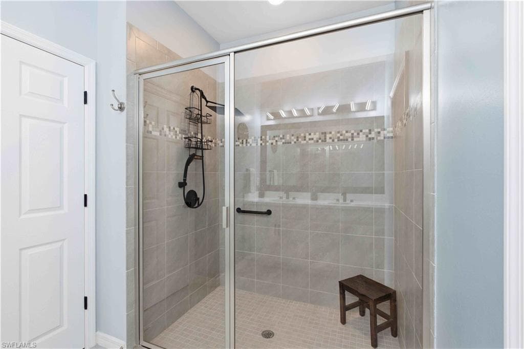 Glass-enclosed shower featuring large format wall tiles, a decorative mosaic tile band, and a textured floor
