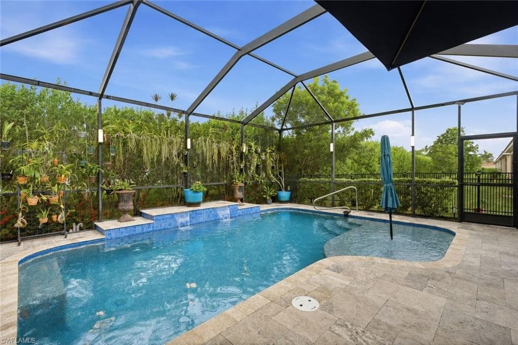 Screen-enclosed pool area featuring a blue-tiled swimming pool with integrated steps, waterfall features, and a spacious paver deck