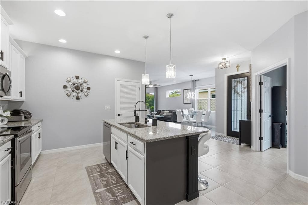 Kitchen featuring an island with a sink, pendant lighting, stainless steel appliances, light-toned cabinetry with dark hardware, and granite countertops
