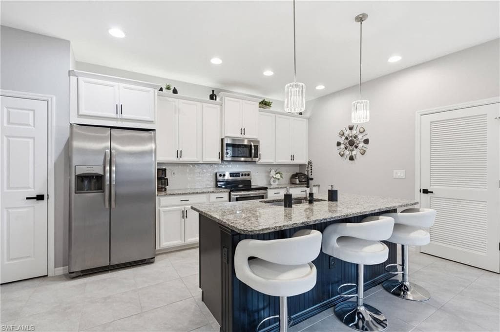 Modern kitchen featuring an island with a light-toned countertop, white cabinetry, integrated stainless steel appliances, a tile backsplash, and recessed lighting