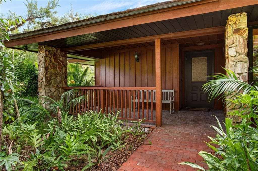 Covered entry porch featuring wood paneling, stone accents, and a brick pathway