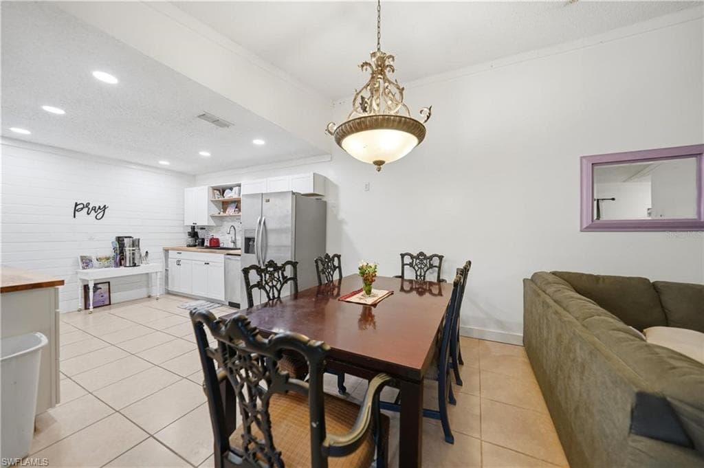 Open-concept space featuring a dining area with a chandelier, a kitchen area with white cabinetry, wood-finish countertops, and stainless steel appliances, and tile flooring throughout