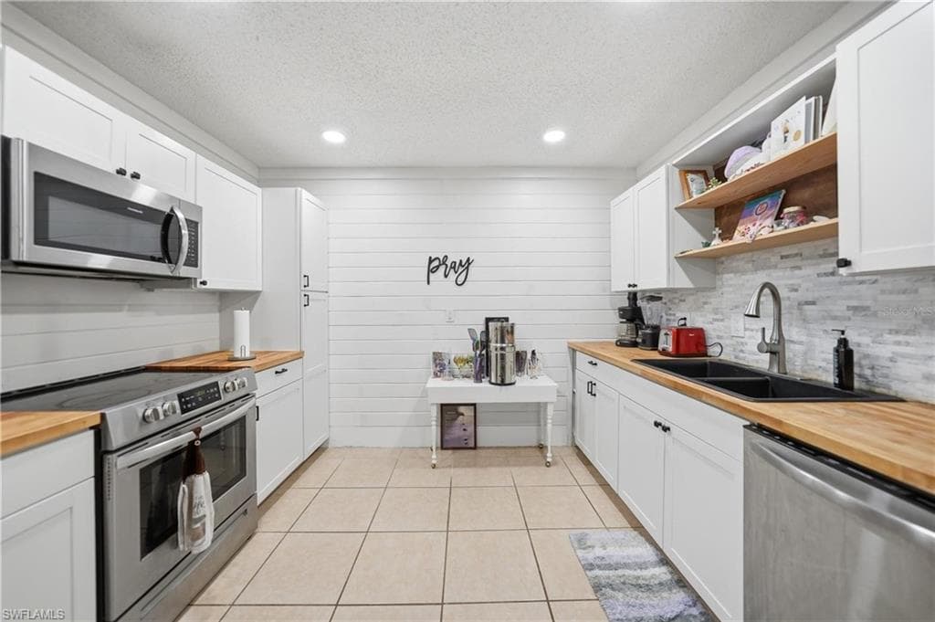 Kitchen with full-height white cabinetry, wood-finish countertops, stainless steel appliances, and tile flooring