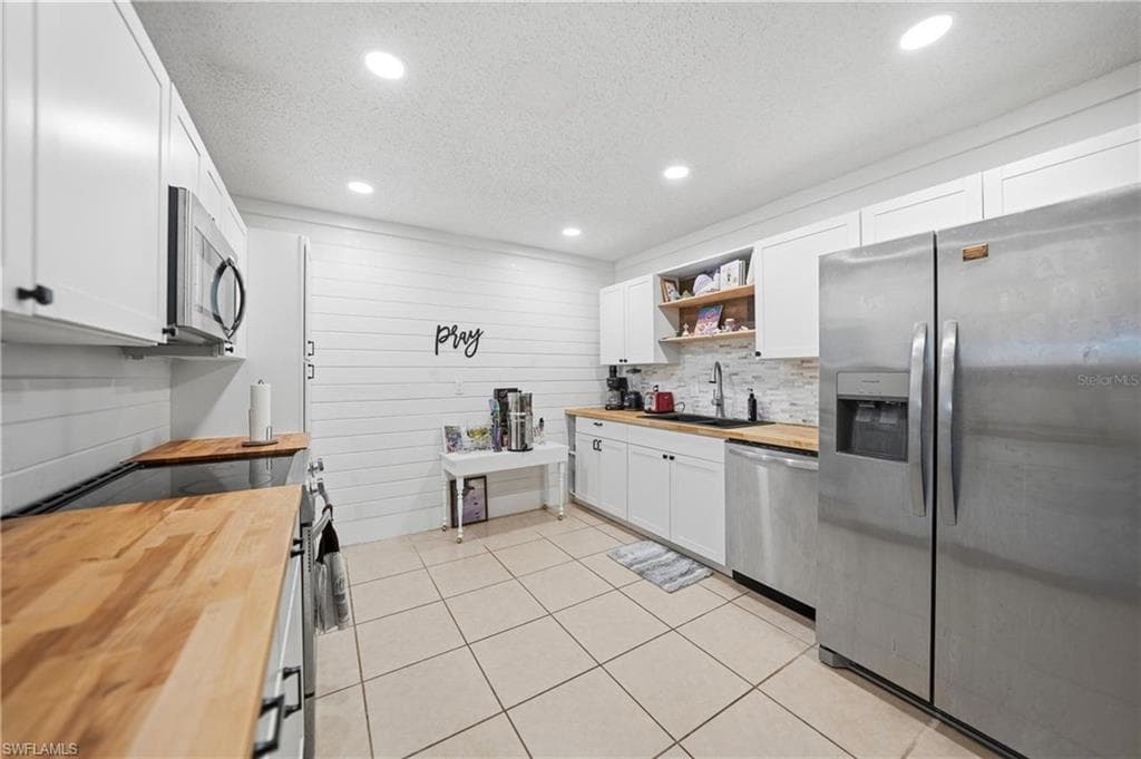 Kitchen featuring wood-finish countertops, white shaker cabinetry, stainless steel appliances, and recessed lighting