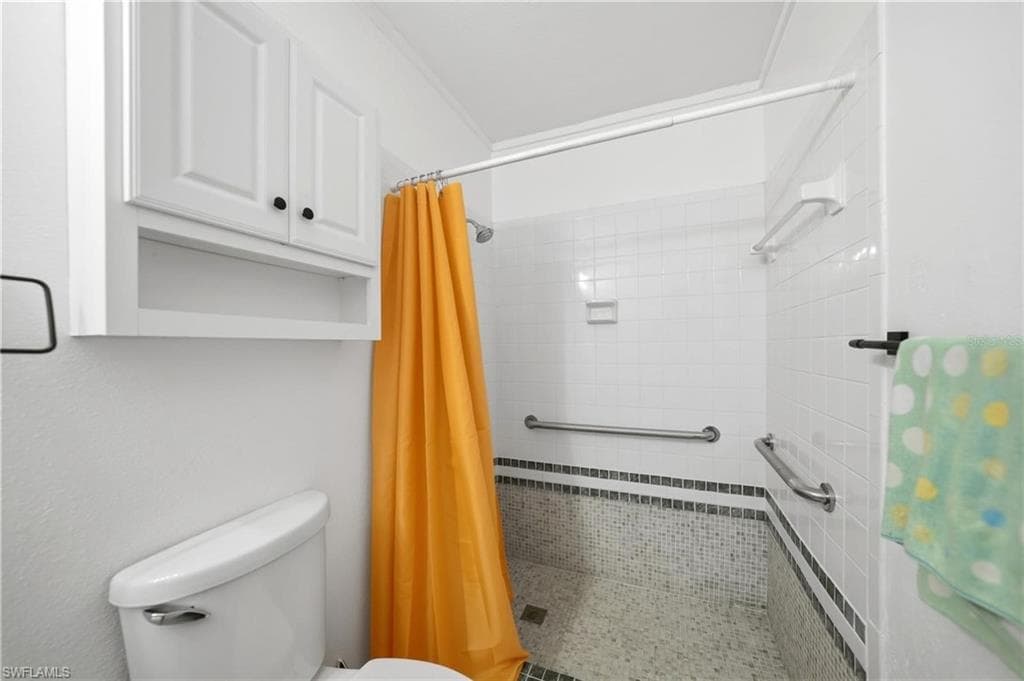 Bathroom featuring a white toilet, built-in white cabinetry, a shower area with white subway tile, and a mosaic tile floor with a decorative border