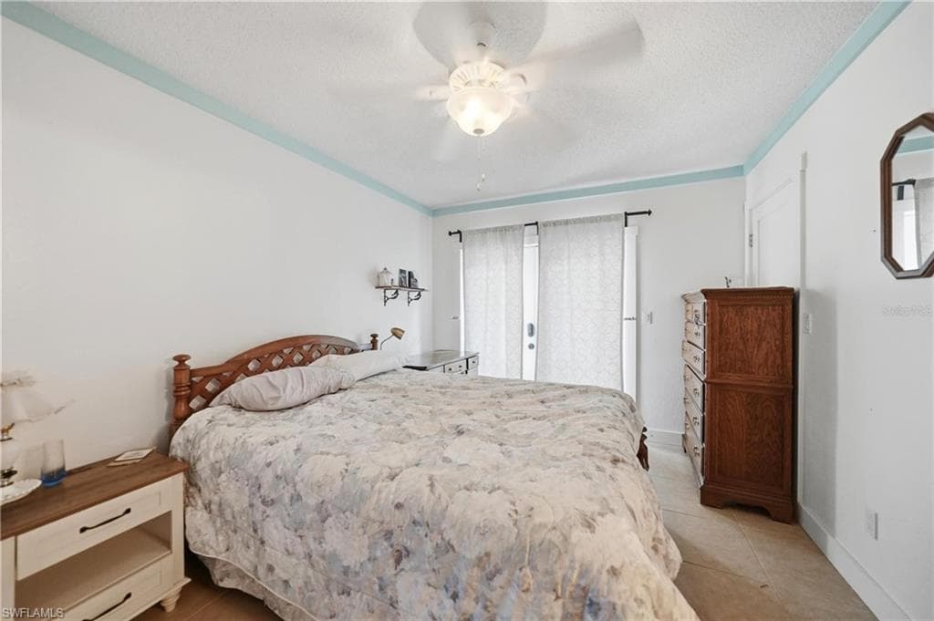 Spacious bedroom featuring light-colored walls with a contrasting blue accent trim, a ceiling fan with integrated lighting, and tile flooring