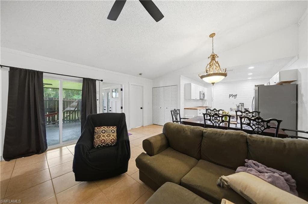 Open-concept living area featuring tile flooring, vaulted ceilings, a ceiling fan, and sliding glass doors to the outdoor patio
