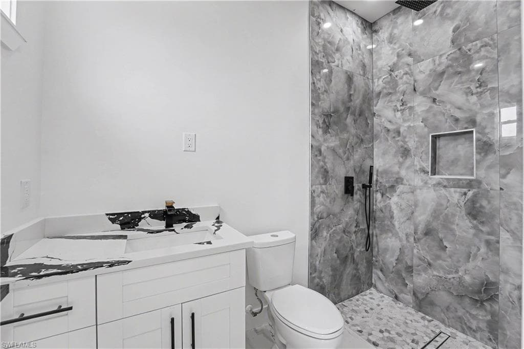 Walk-in shower with large-format gray marble-patterned wall tiles, pebble-style floor, and matte black fixtures