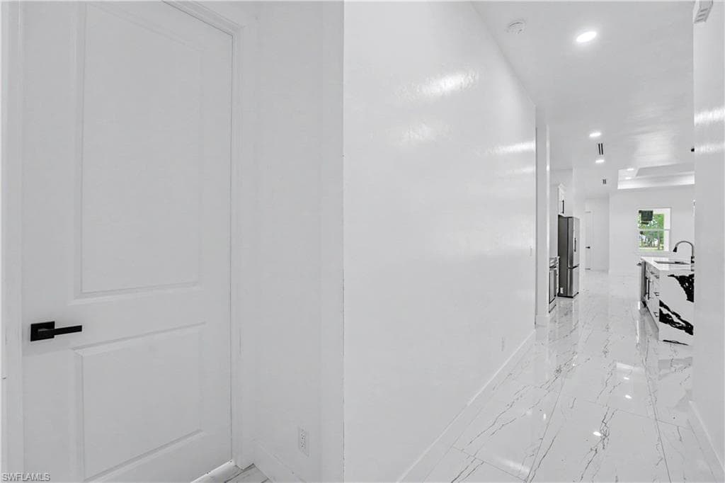 Hallway featuring white walls, recessed lighting, and large format white tile flooring with dark veining