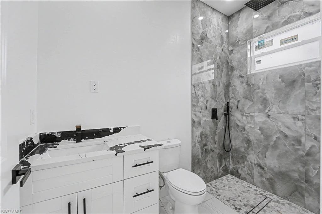 Bathroom featuring a white vanity with black hardware, a wall-mounted faucet, and a shower with large format marble-look tile walls