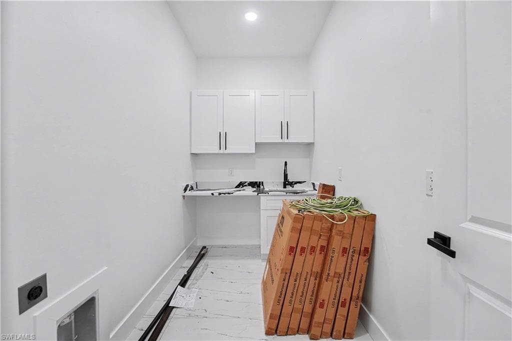 Utility room featuring white shaker cabinetry, a sink with a matte black faucet, and a wall-mounted light fixture