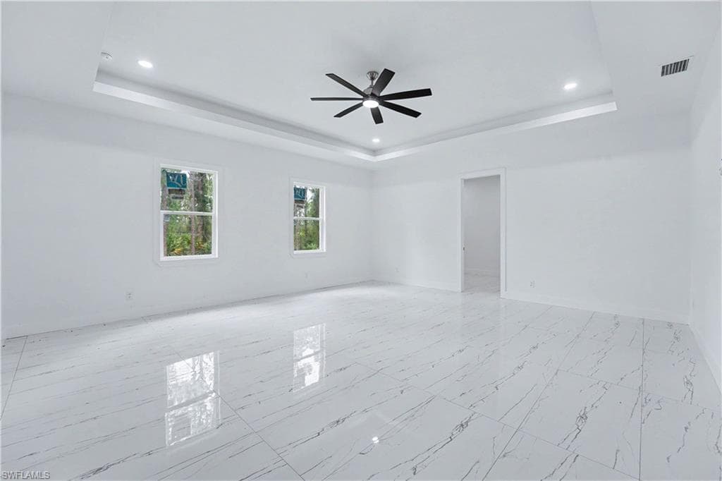 Spacious room featuring white walls, large format tile flooring, and a tray ceiling with recessed lighting