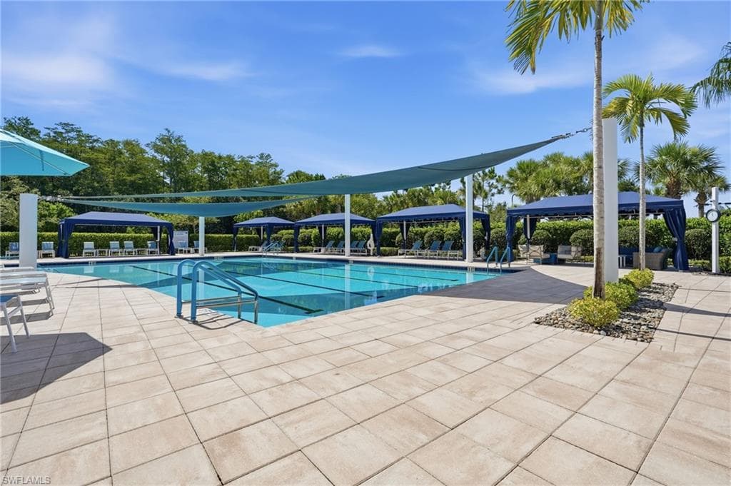 Outdoor lap swimming pool with sun shade, surrounded by paver decking, multiple private cabanas, and beautiful landscaping.