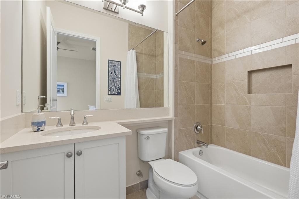 Bathroom featuring a white vanity with a large mirror, a built-in tub with a shower and light-toned tile surround with a decorative accent band and recessed niche.