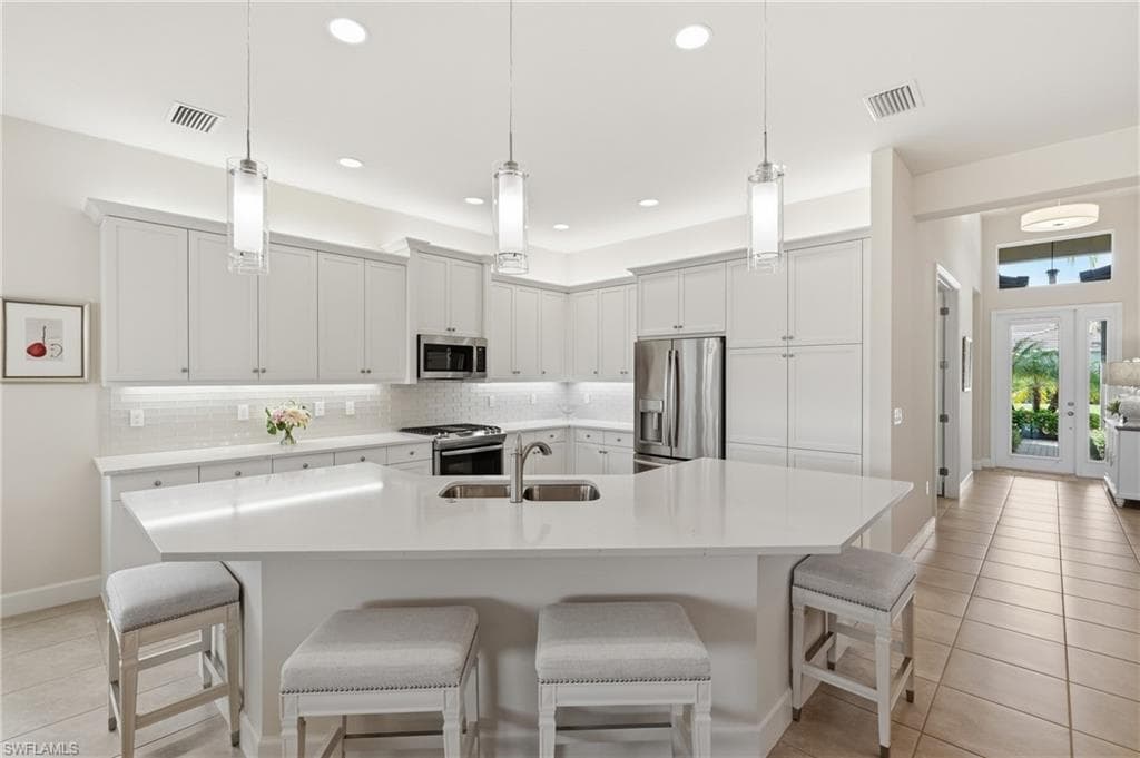 Kitchen featuring a large island with quartz countertops, white cabinetry with crown molding and pendant lighting.