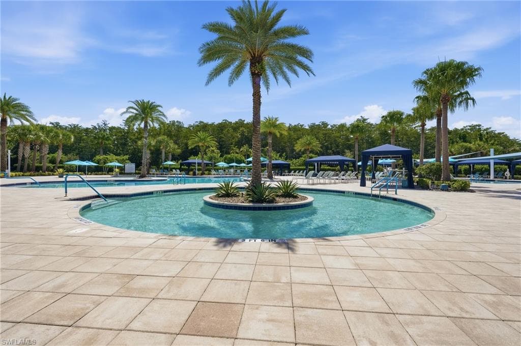 Resistance pool with an island palm tree, surrounding tiled patio, additional pools and multiple shaded cabanas.