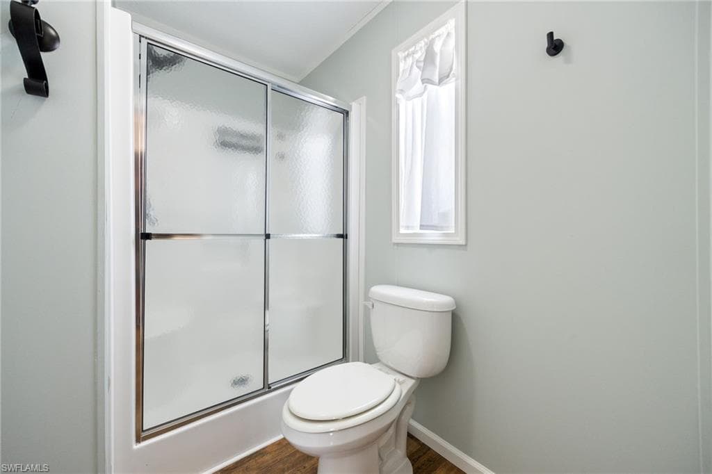 Master bathroom featuring a walk-in shower with sliding glass doors, white toilet, window with white trim, and wood-finish flooring.