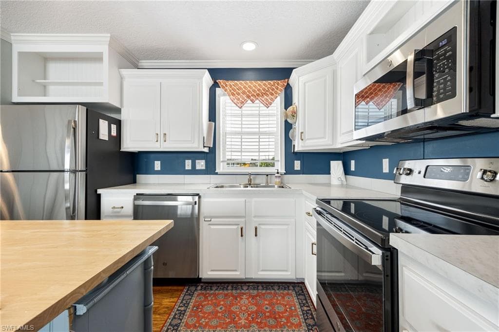 Kitchen featuring white cabinetry, light-colored countertops, stainless steel appliances, a built-in microwave, and wood-finish flooring.