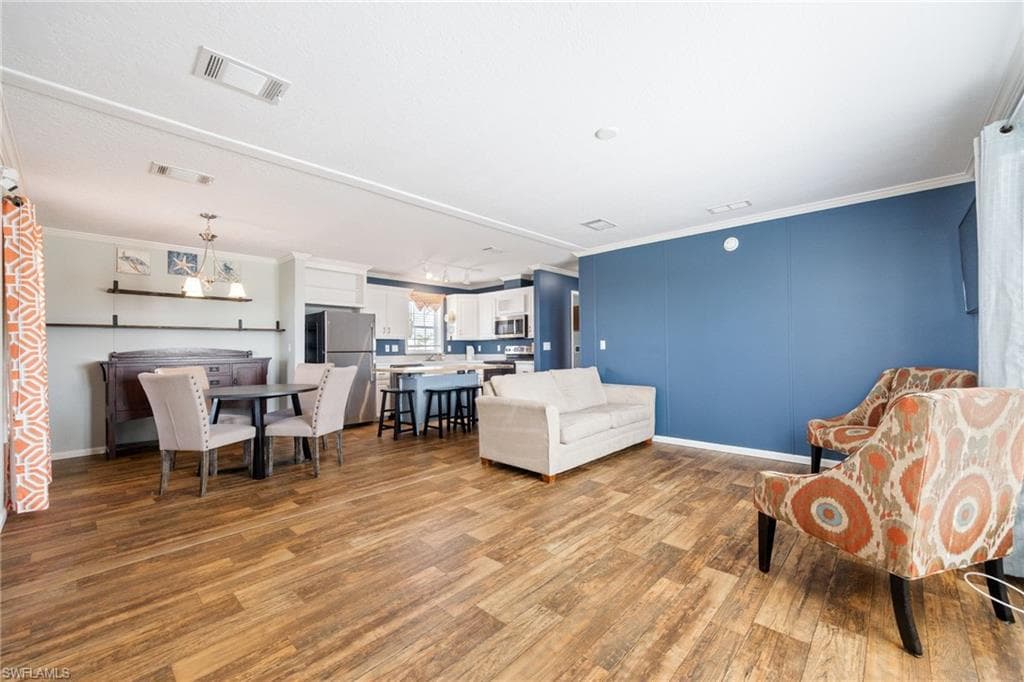 Open-concept living space featuring wood-finish flooring, white crown molding, and a vibrant accent wall.