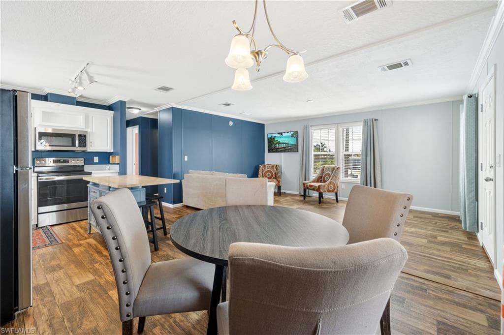 Open concept interior featuring wood-finish flooring, white cabinetry, stainless steel appliances, and a central island with countertop seating.