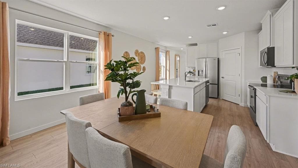 Open-concept living space featuring wood-finish flooring, recessed lighting, and a kitchen with white cabinetry, a center island with a sink, and stainless steel appliances