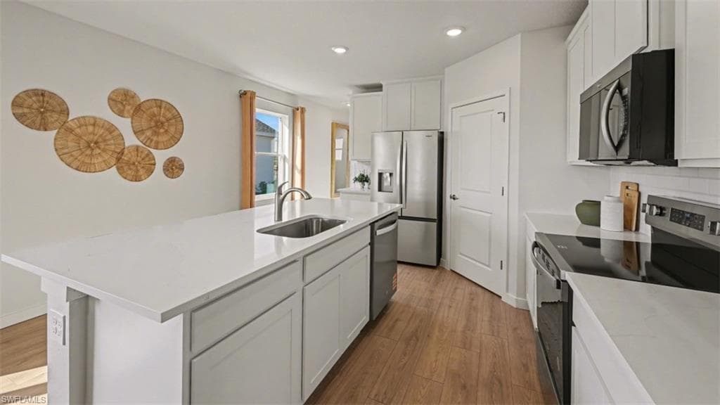 Modern kitchen featuring white cabinetry, a large kitchen island with an undermount sink, stainless steel appliances, and wood-finish flooring