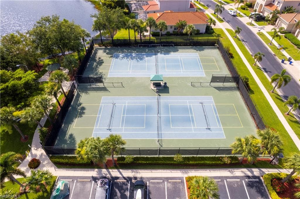 Multiple tennis courts featuring a green and blue playing surface, black perimeter fencing, and a central shaded seating area