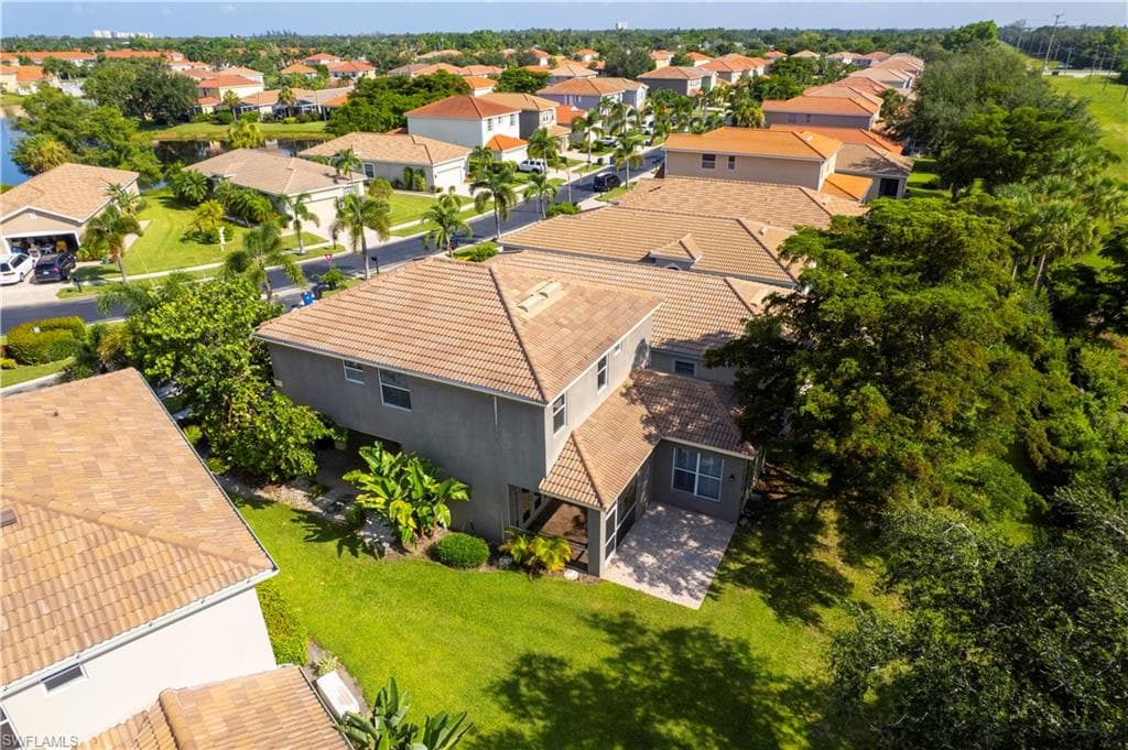 Aerial perspective showcasing a tiled-roof residence with a screened patio and private backyard, surrounded by lush landscaping and a manicured lawn