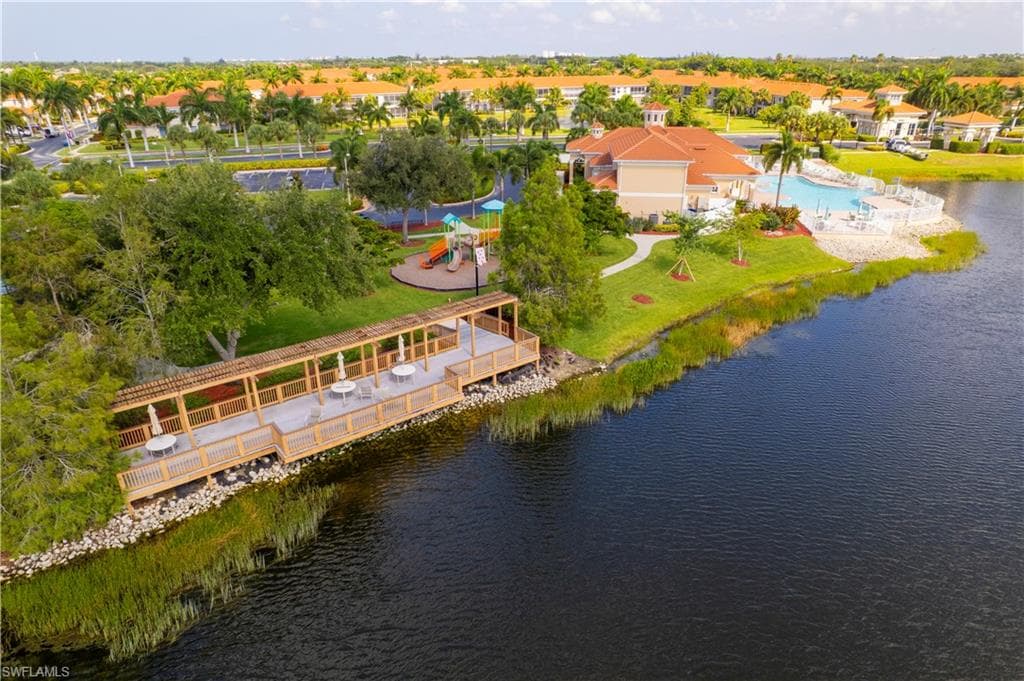 Gated community entrance featuring Mediterranean-style architecture, lush tropical landscaping with mature palm trees, a water feature with fountain, and paved roadways with manicured grass medians