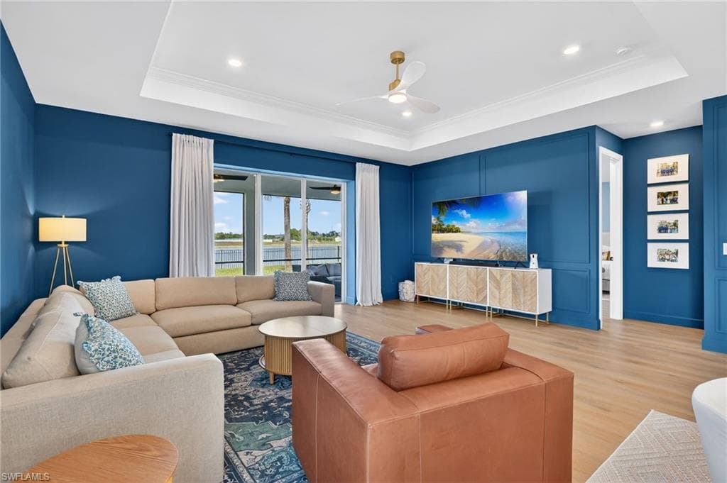 Spacious living area featuring custom wall paneling, light wood-finish flooring, and a tray ceiling with crown molding