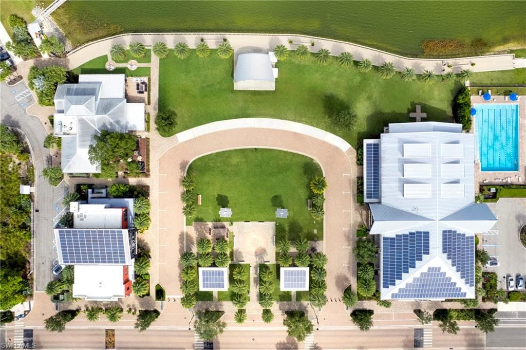 Aerial perspective showcasing multiple properties, extensive green spaces, a large outdoor swimming pool, paved pathways, and numerous solar panels visible on several rooftops