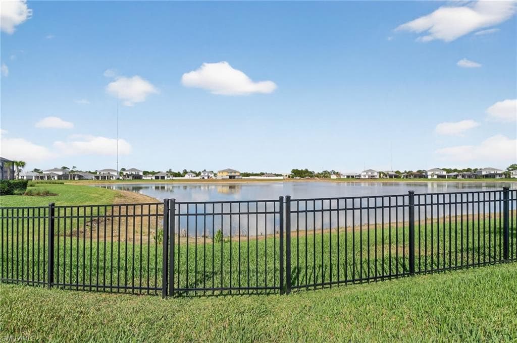 Expansive waterfront property featuring a black metal fence and mature green lawn
